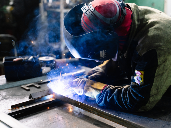 Welder wearing protective gear welding metal components in a workshop
