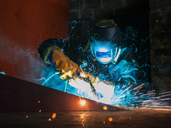 Welder wearing protective gear welding metal components with bright sparks
